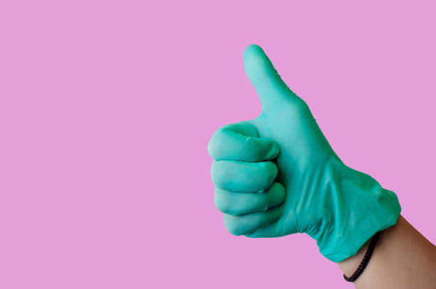 istock Female hand in blue latex glove makes thumbs up like gesture isolate on a light pink background. Medical health concept. Copy space 1171301656