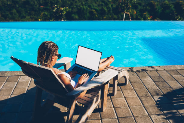 istock Young woman in sunglasses doing remote work at modern laptop with blank copy space screen for your internet content while resting on sunbed near blue swimming pool enjoying summer vacation 1171303048