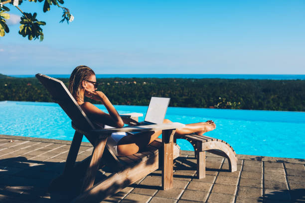 istock Pensive slim young woman working freelance at netbook with blank screen area while resting on sunbed near swimming blue poor enjoying summer resort.Tourist reading news on laptop while sunbathing 1171303049