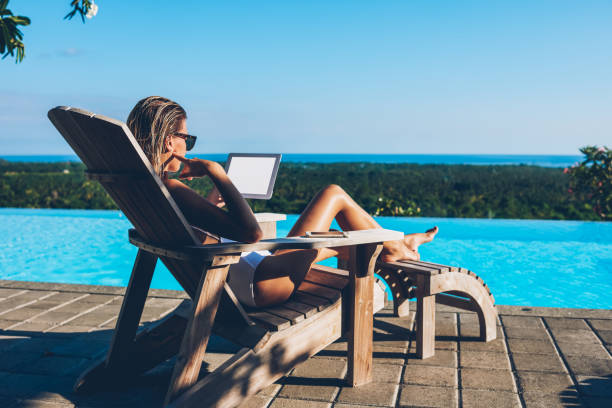 Pensive young woman in sunglasses reading email and working remotely using modern tablet with blank screen area for your advertising content while relaxing on sunbed after swimming in blue pool mujer joven pensativa en gafas de sol leyendo correo electrónico y trabajando remotamente usando tableta moderna con área de pantalla en blanco para su contenido publicitario mientras se relaja en la tumbona después de nadar en la piscina azul