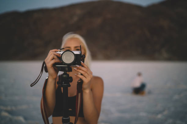 istock Selective focus on modern digital camera for shooting landscape in Badwater basin during evening dusk,female photographer taking picture using tripod traveling for work in Death valley national park 1171307241