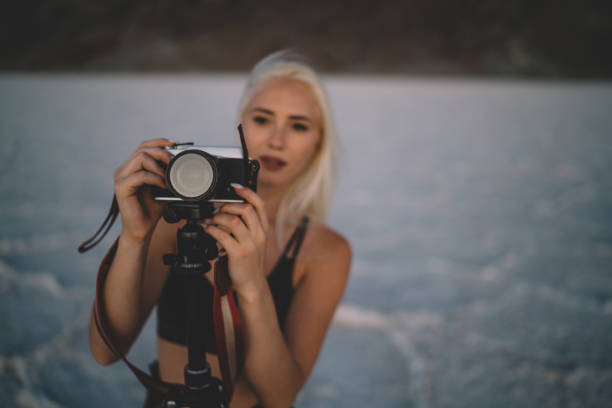 istock Selective focus on camera standing on tripod for shooting wild environment of Badwater basin, Blurred female tourist photographer taking picture of landscape with dry surface suring working expedition 1171307250
