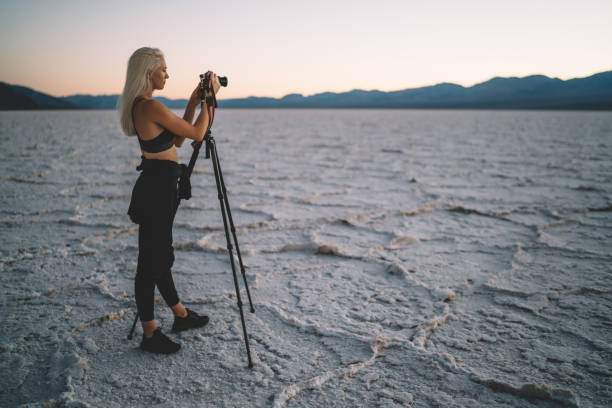 istock Young female photographer shoot sunset in Death Valley using digital camera and tripod, tourist woman making pictures of wild landscape of Badwater basin in evening dusk having journalistic expedition 1171307252