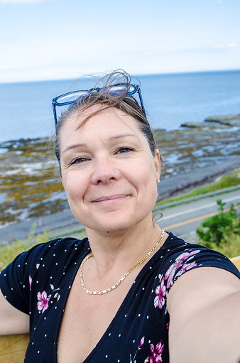 Woman taking selfie in front of sea of La Martre (Gaspesie)  during summer day