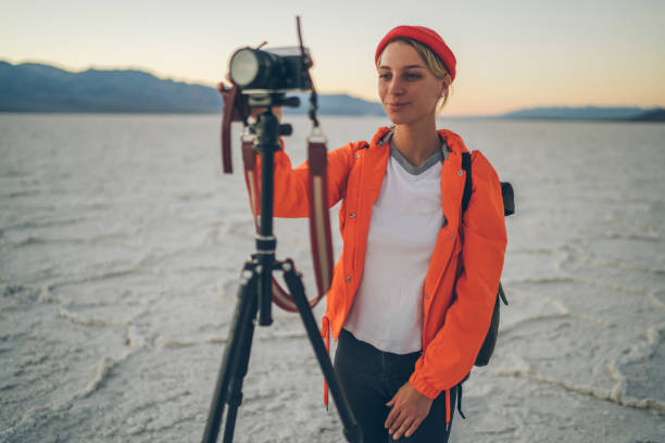 istock Positive skilled woman making settings on camera waiting for sunset for shooting video in desert during journey, professional female photographer taking pictures of nature and landscape via tripod 1171307412