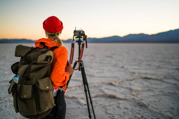 istock Hipster girl with touristic backpack using professional equipment for taking photos in evening desert, back view of young woman photographer standing near tripod with camera for making pictures 1171307429