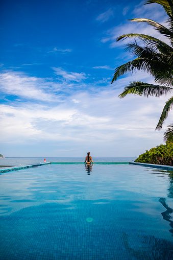 Woman relaxing in infinity swimming pool with sea view, vacation in tropical country