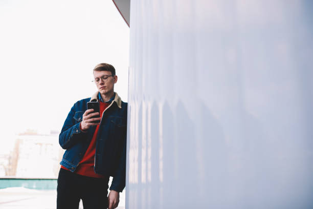 istock Stylish dressed young hipster blogger chatting in social networks using high speed internet connection on smartphone device standing near wall with copy space area for advertising text message 1171307503