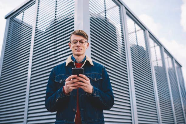 istock Successful hipster blogger laughing during friendly messaging in social networks on smartphone connected to 4 internet.Positive young man updating profile on telephone standing in urban setting 1171307511