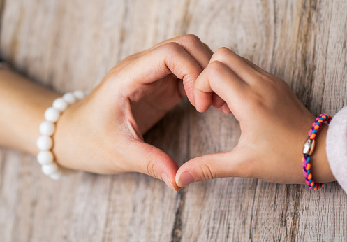 Cropped hands of mother and daughter making heart shape on table. High angle view of cocktail at cafe. They are bonding at coffee shop.