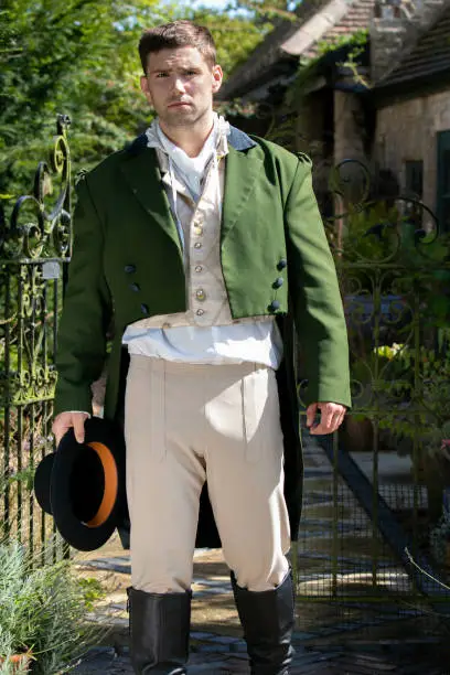 Photo of Portrait of handsome gentleman dressed in vintage costume, holding top hat in stately home courtyard