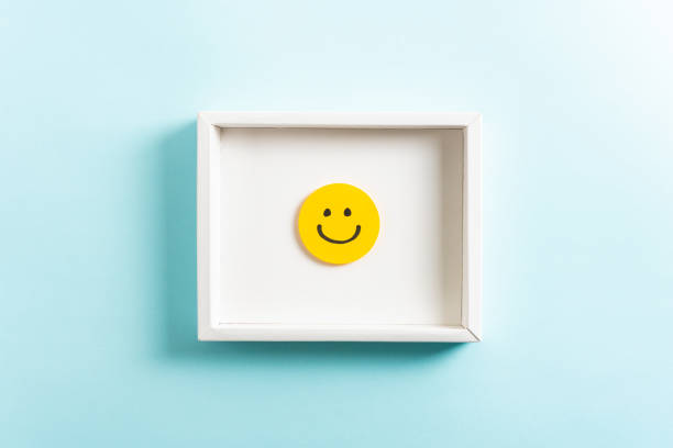 Happy diploma concept. Concept of well-being, well done, feedback, employee recognition award. Happy yellow smiling emoticon face frame hanging on blue background. stock photo