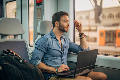 Man sitting in train by the window and working on laptop computer