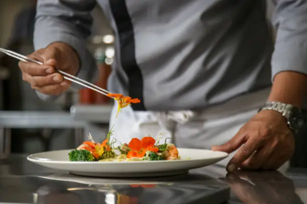 Photo of Closeup of male chef arranging edible flowers on the meal in the commercial kitchen