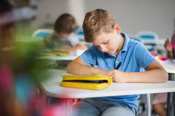 istock A small school boy sitting at the desk in classroom, writing. 1171340476