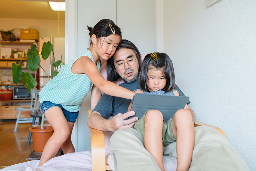 A modern father is using a digital tablet with his daughters.