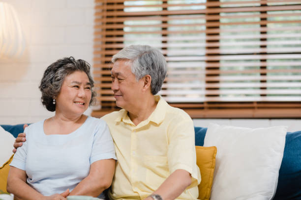 couples âgés asiatiques retenant leurs mains tout en prenant ensemble dans le salon, le couple se sentant la part heureuse et soutiennent l'un l'autre se trouvant sur le sofa à la maison. concept de famille aînée de style de vie à la maison. - mental illness energy people men photos et images de collection