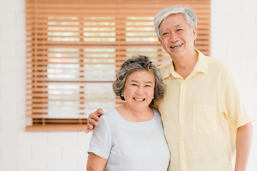 Asian elderly couple feeling happy smiling and looking to camera while relax in living room at home. Enjoying time lifestyle senior family at home concept. Portrait looking at camera.