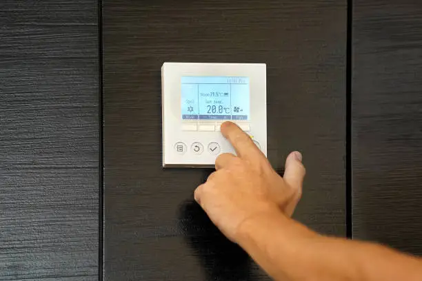 Male hand try to turn on the new air condition in room, in the hotel room. Caucasian man hands on the air conditioning control panel. Hand setting temperature air condition.