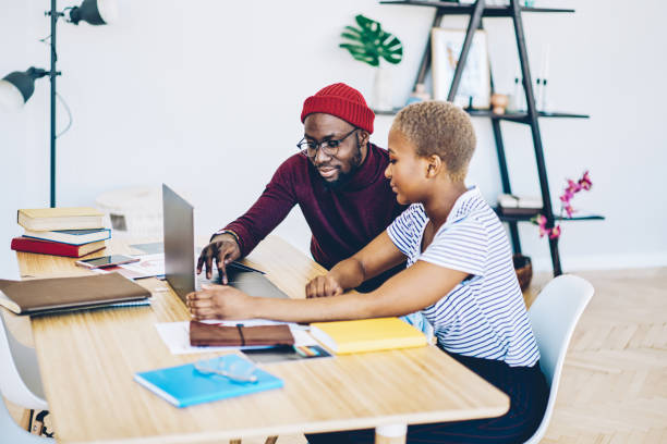 istock Serious dark skinned hipster guy installing application on laptop computer of his female colleague sitting at desktop, african american couple making booking together  browse web page on netbook 1171354221
