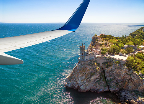 Crimea - May 19, 2016: Plane flies above Crimea, Russia. Aerial panoramic view of Swallow's Nest castle and wing from airplane window. The plane's flight over Black Sea. Concept of vacation and summer travel in Crimea.