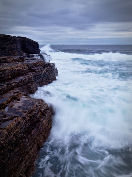 Waves crashing on the rocky cliffs of the Irish west coast at dusk (long exposure) stock photo