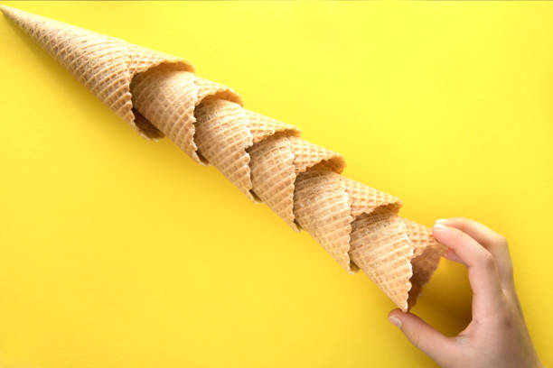 istock Children's hand pulls one empty waffle cup for ice cream. Waffle cups lie diagonally on a yellow background and a children's hand pulls one of them. 1171374741