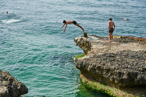 Beirut, Lebanon - April 29, 2019: a young lebanese adult plunge into mediterranean sea from a rock along Corniche El Manara. Beirut Central District.