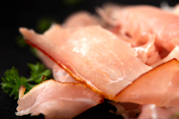 istock Thin sliced smoked pork ham on a dark slate with herbs 1171378236