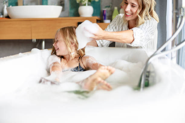 Cute girl is squinting eyes in the bath Happy mom holding foam in her hands stock photo girls bath stock pictures, royalty-free photos & images