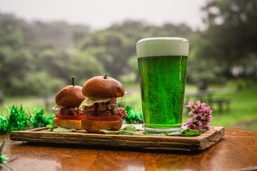Green colored beer standing next to mini burgers for St. Patrick`s Day