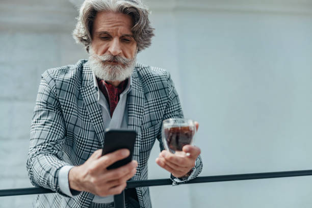 istock Serious bearded gentleman with drink using mobile phone 1171393616