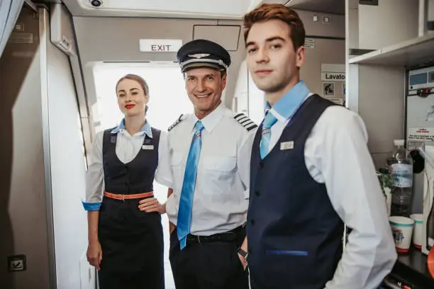 Photo of Smiling Caucasian pilot with flight attendants standing on airplane board