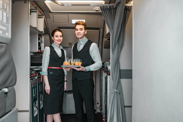 Smiling flight attendant with pilot posing for camera Caucasian stewardess standing with her colleague near door of airliner stock photo. Airways concept crew stock pictures, royalty-free photos & images