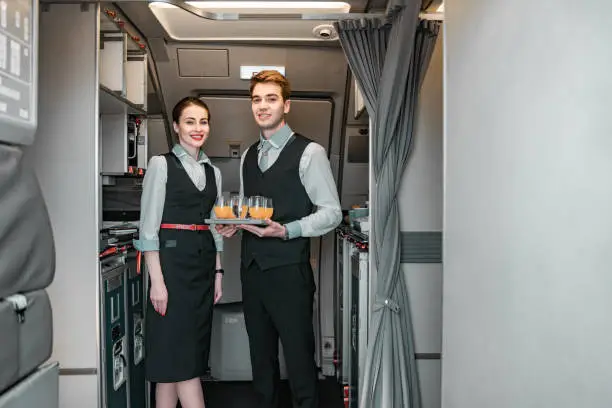 Caucasian stewardess standing with her colleague near door of airliner stock photo. Airways concept