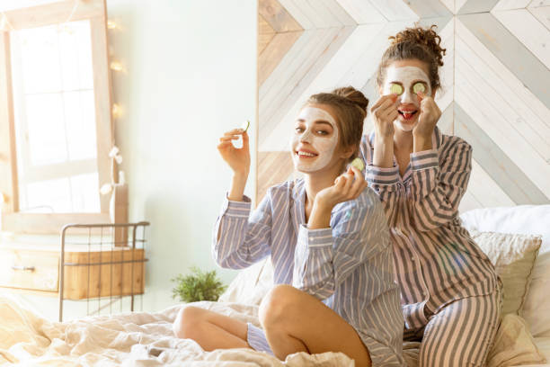 dos chicas amigas bonitas que tienen el día del spa - facial mask spa treatment cucumber human face fotografías e imágenes de stock