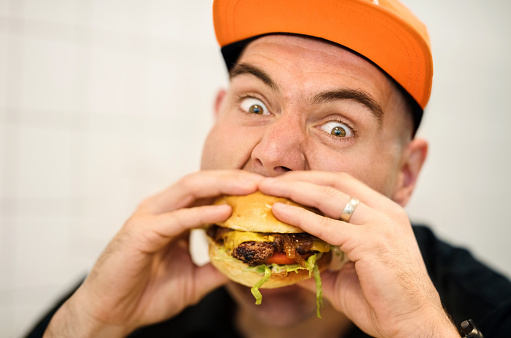 Close up of a hungry man wearing cap eating a burger