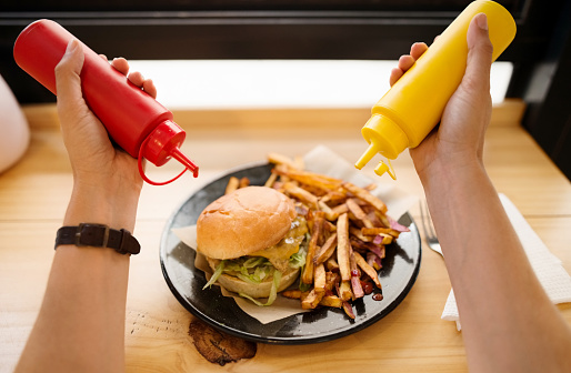Point of view shot of a woman adding mustard and ketchup to burger and french fries at a restaurant