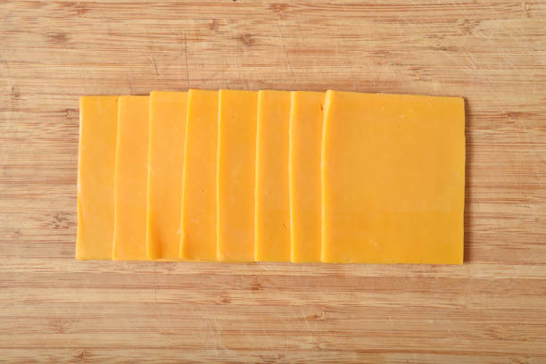 Sliced cheddar cheese on a cutting board Overhead view of cheddar cheese slices on a cutting board cheddar cheese photos stock pictures, royalty-free photos & images