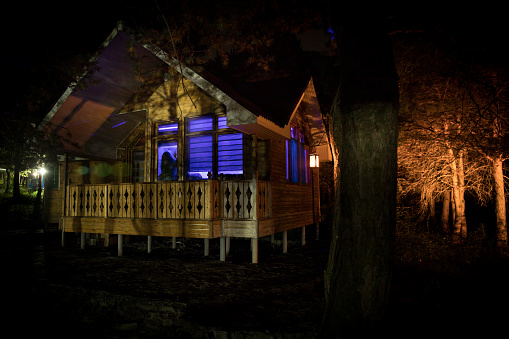 Old house with a Ghost in the forest at night. Horror silhouette at the window. Old building in forest. Surreal lights. Horror Halloween concept