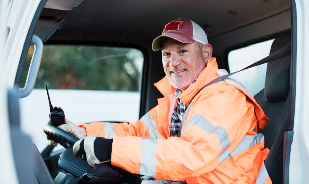 Hispanic man driving a truck A truck driver sitting in his vehicle, looking at the camera through the open driver's side door. He is wearing reflective clothing a plaid shirt and trucker's hat, holding a walkie-talkie. He is a mature Hispanic man in his 50s. one mature man only audio stock pictures, royalty-free photos & images