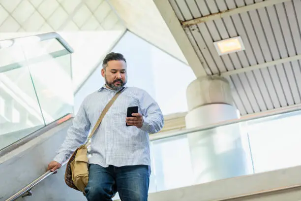 Photo of Hispanic man walking, looking at mobile phone