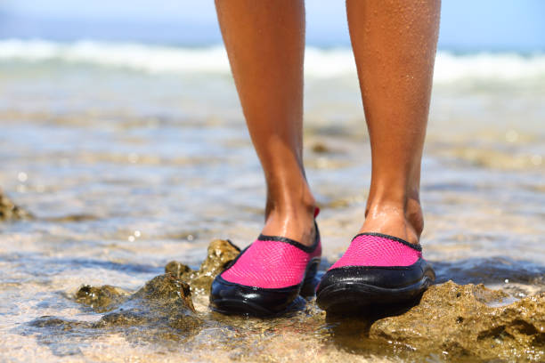 Water shoes / swimming shoe in red neoprene Water shoes / swimming shoe in Pink neoprene on rocks in water on beach. Closeup detail of the feet of a woman wearing bright pink neoprene water shoes standing on rocks at the edge of the ocean. neoprene photos stock pictures, royalty-free photos & images