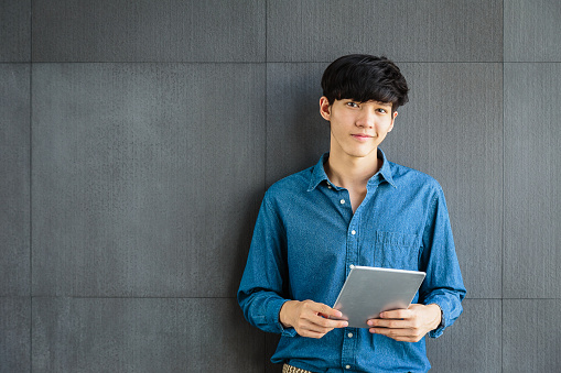 Portrait of young smiling Asian Business man holding digital tablet computer on gray background, Looking at camera