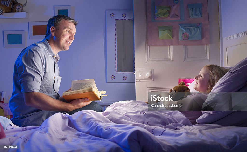 bedtime story dad reads his daughter a story from a well worn story book  . Bed - Furniture Stock Photo