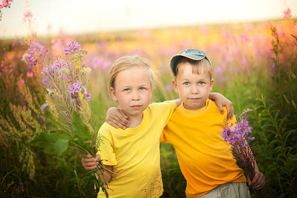 A smiling African American father carries his daughter on his back as they walk through tall wildflowers at sunset. Warm, playful outdoor moment showcasing family, togetherness, and carefree fun.
