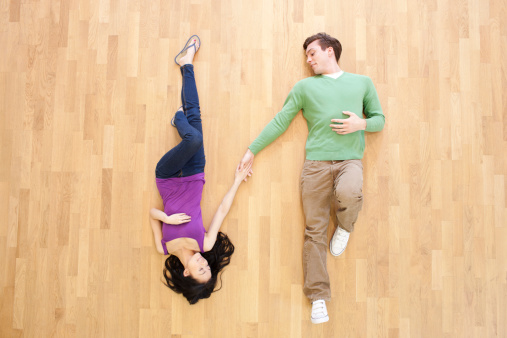A young couple, lying on a wooden floor, holding hands.