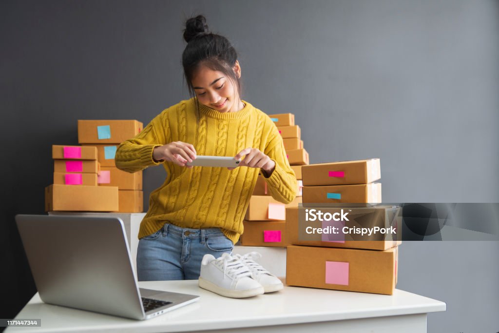 Young women taking photo to shoes with cell telephone or smartphone digital camera for post to sell online on the Internet and preparing pack product box. Selling online ideas concept Internet Stock Photo