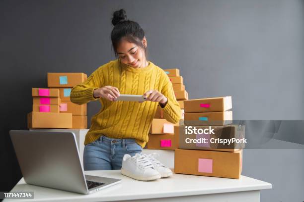 Young Women Taking Photo To Shoes With Cell Telephone Or Smartphone Digital Camera For Post To Sell Online On The Internet And Preparing Pack Product Box Selling Online Ideas Concept Stock Photo - Download Image Now