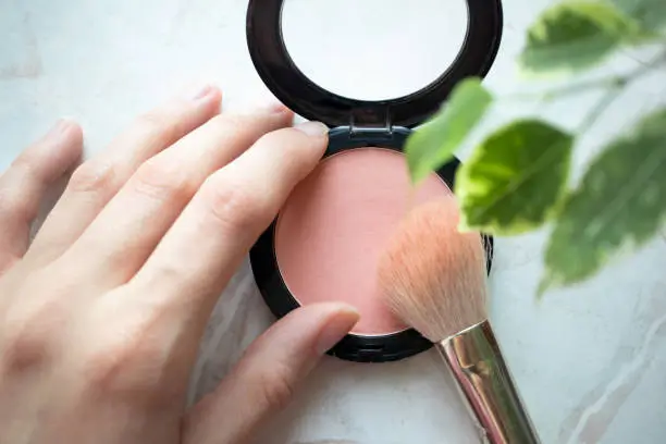 Female hand holding opened blush powder and brush in interior. Top view, Close-up, make-up concept